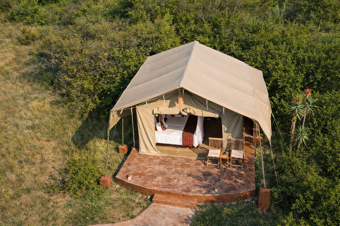 A canvas safari tent with a stone verandah set among green bush in the Maasai Mara