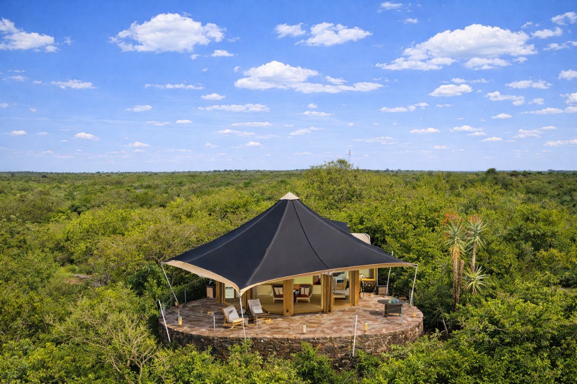 A tented safari camp room with a canvas roof and open front looking out over dense green bush